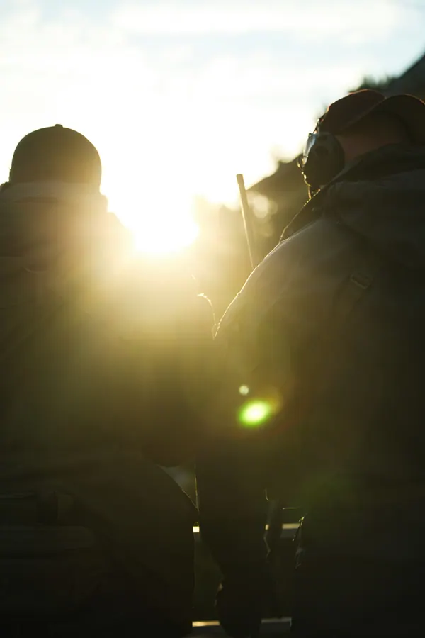 Two operators against the low sun, headsets and packs reduced to outline