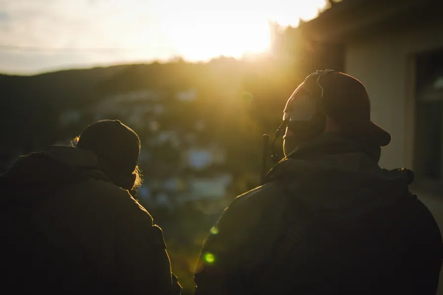 Two operators from behind at last light, headsets and packs against the sun