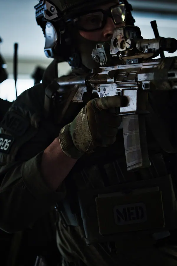 Operator shouldering the rifle indoors, carrier and magazines lit from the window