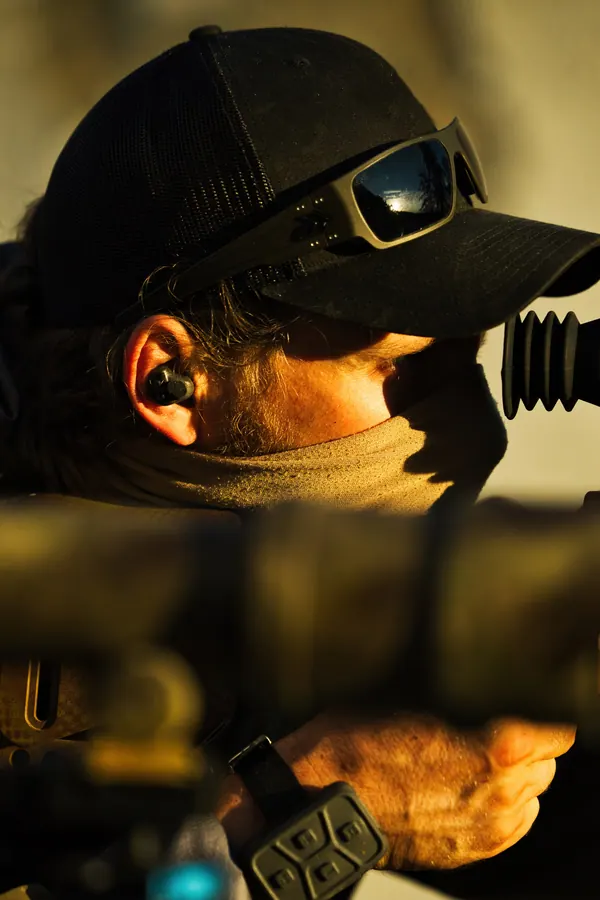 Close on the shooter behind the scope, cap, comms and neck gaiter