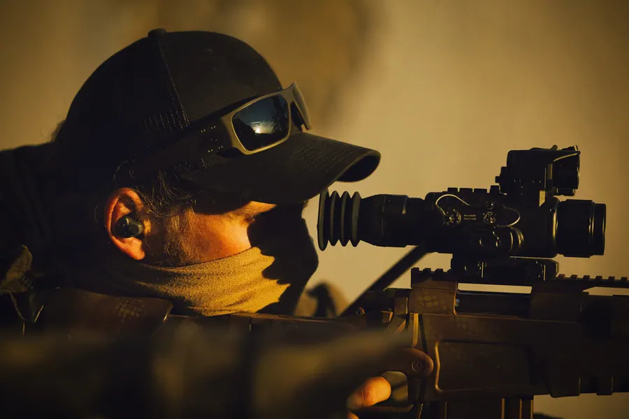 Marksman in warm evening light, eye behind the optic, thermal sight fitted