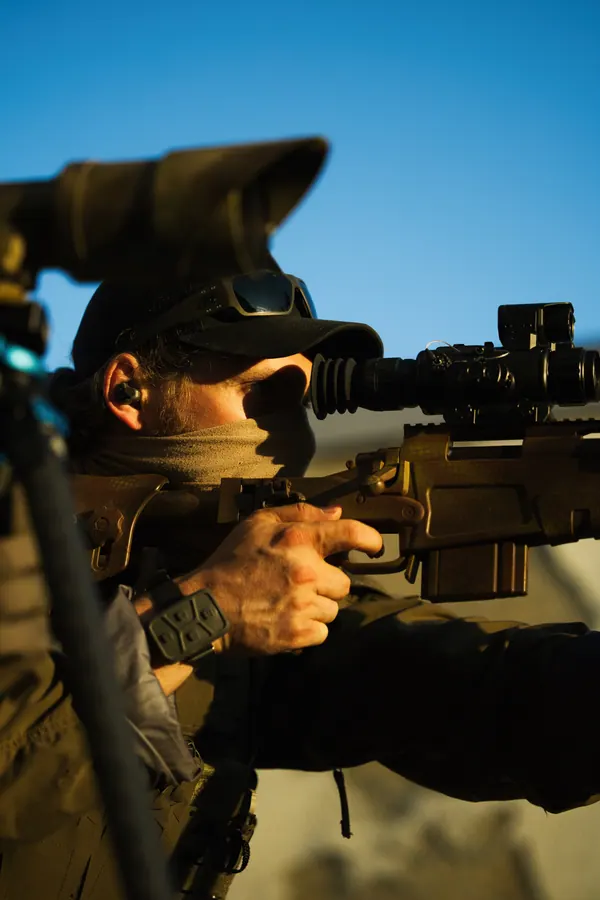 Marksman against open sky, rifle supported, eye behind the optic