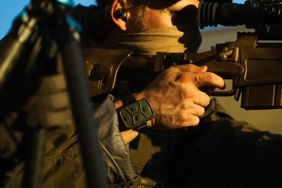 Hands working the bolt on a supported rifle, thermal sight on the rail