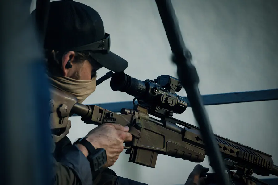 Shooter working the bolt at a supported position, thermal sight mounted on the rail