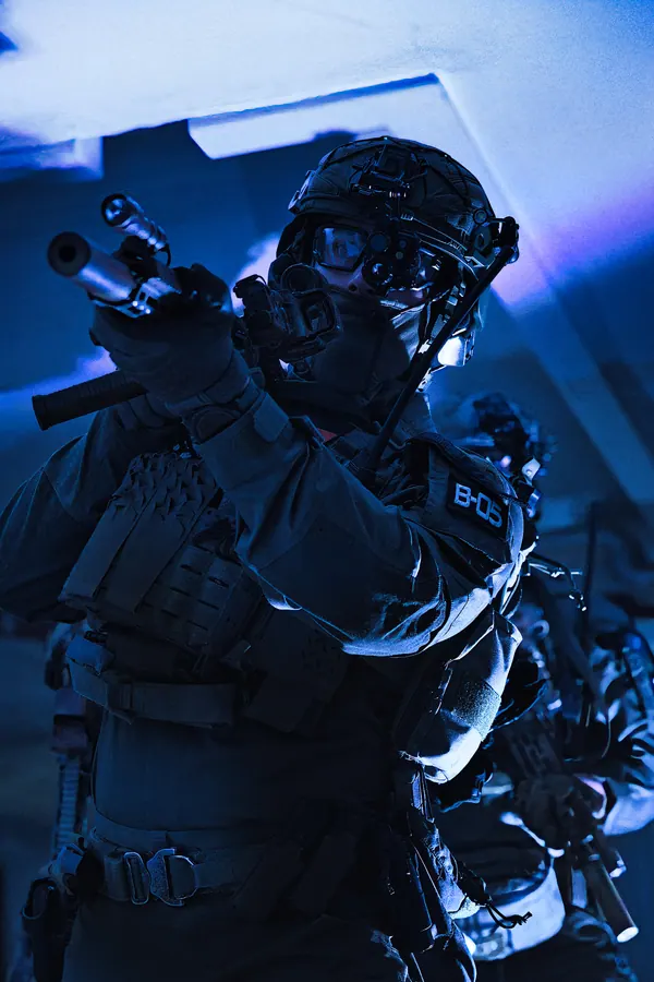 Operator with night vision down, rifle raised in a blue lit room