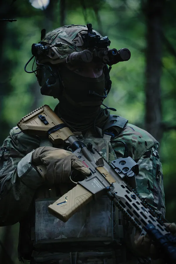 Operator in woodland with night vision mounted, rifle across the body