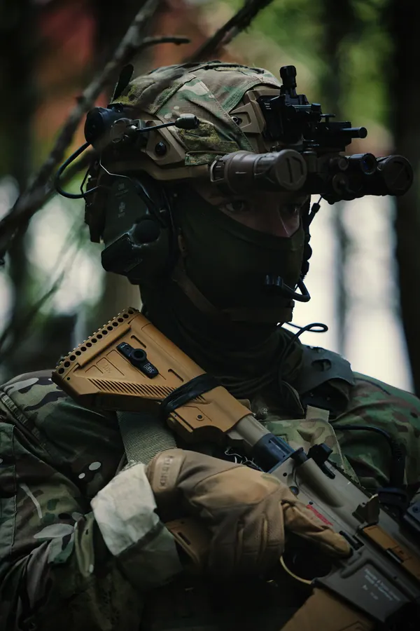 Operator in woodland with quad tube night vision raised, rifle across the chest