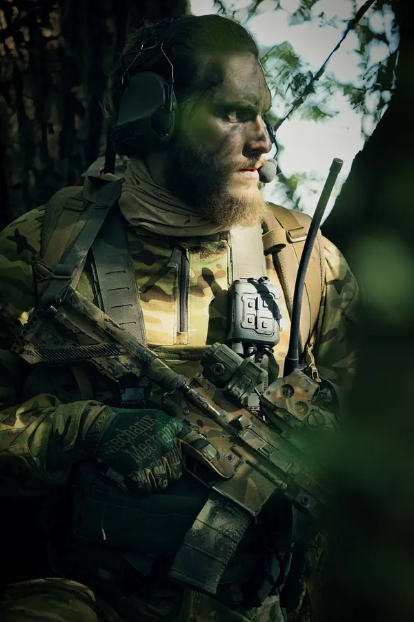 Operator in woodland at rest, face paint and plate carrier in green light