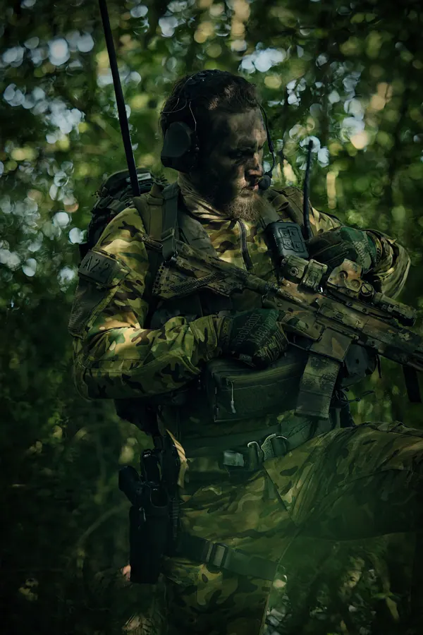 Operator in dense green undergrowth, weapon slung