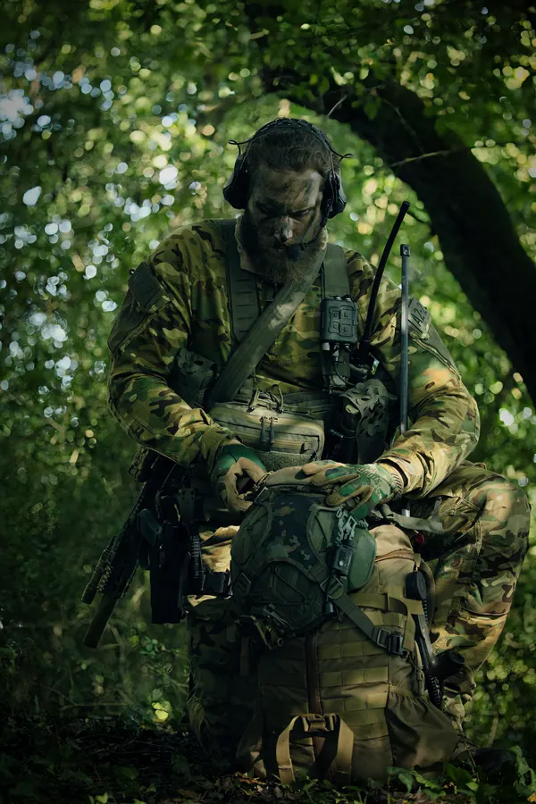 Operator standing in dense woodland, radio and pouches visible on the carrier