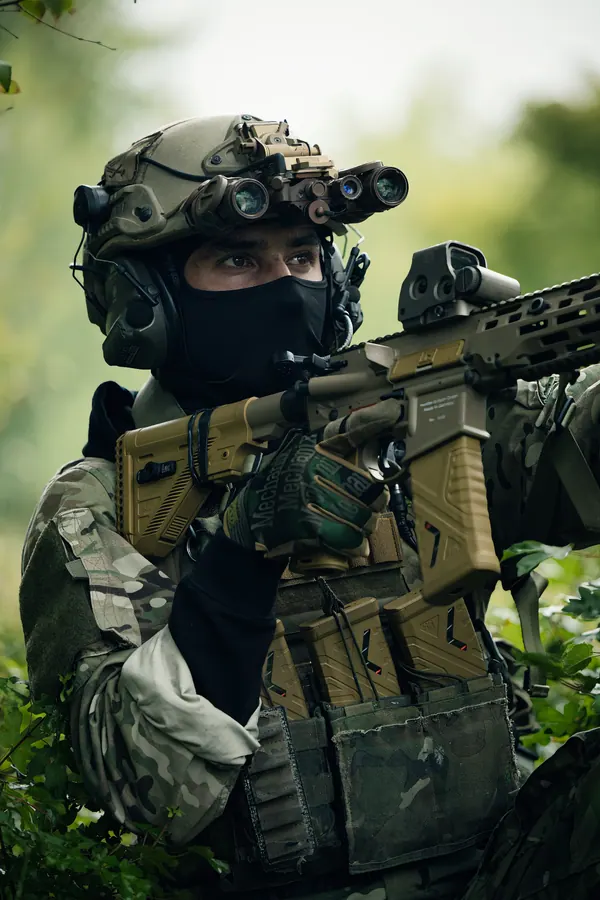 Operator in green woodland with night vision mounted on the helmet, rifle shouldered