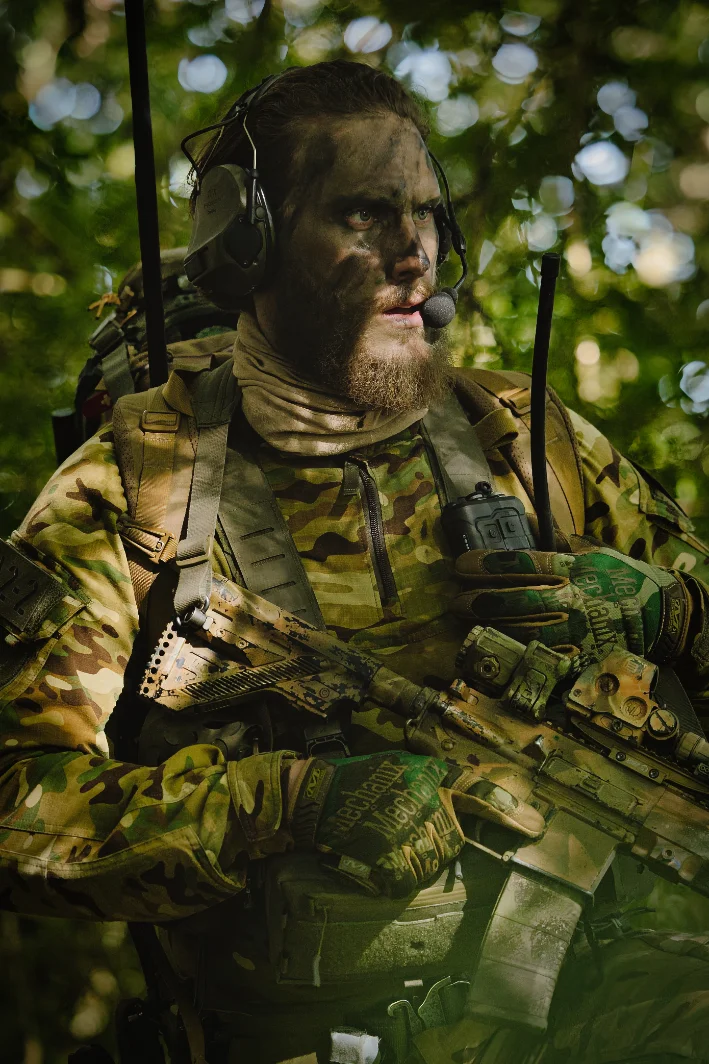 Operator with face paint, headset and boom microphone in green woodland, radio mounted on his chest